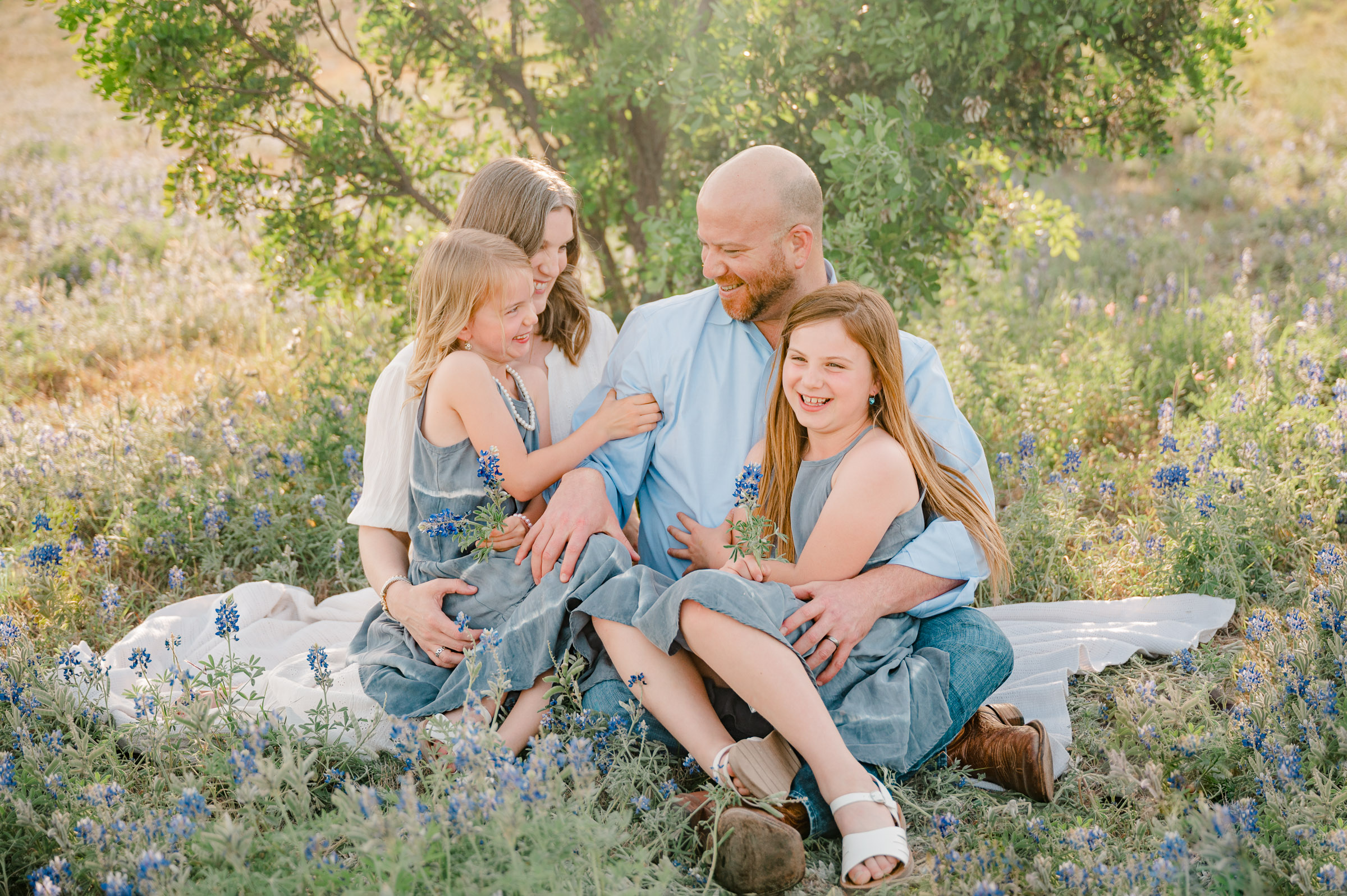 A family plays together on a blanket in a bluebonnet field during family pictures.