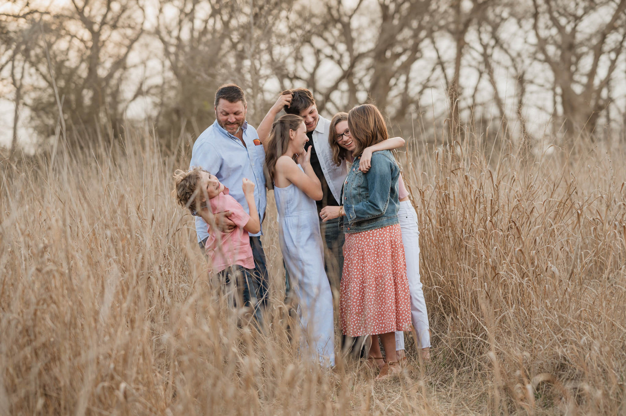 A large family laughs together in a field of tall golden grasses at Cibolo Center for Conservation in Boerne, Texas.