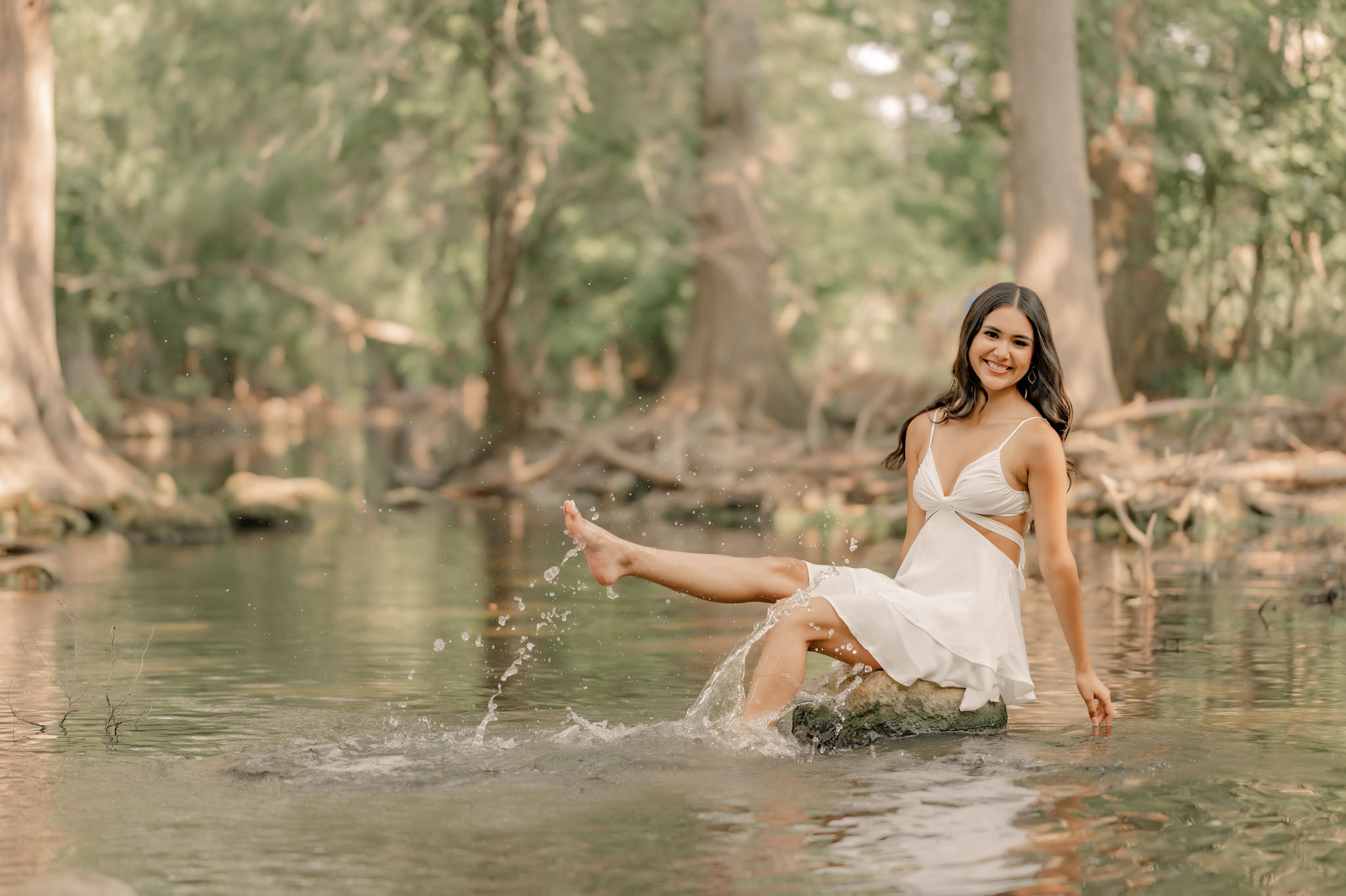 A young woman sits on a stepping stone in Cibolo Creek Nature Center and splashes with her foot.