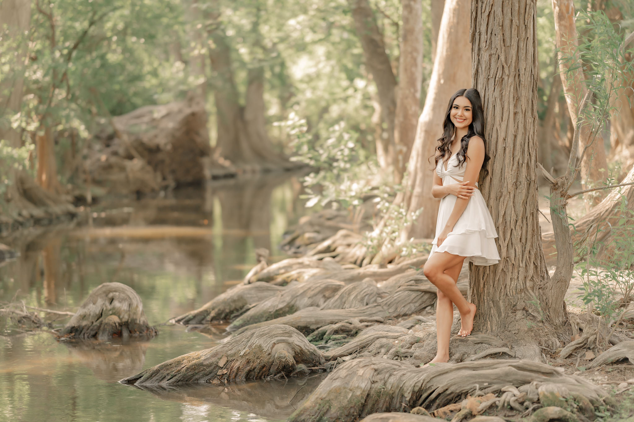 A young woman in a white sundress leans against a tree in Cibolo Center for Conservation in Boerne, Texas.