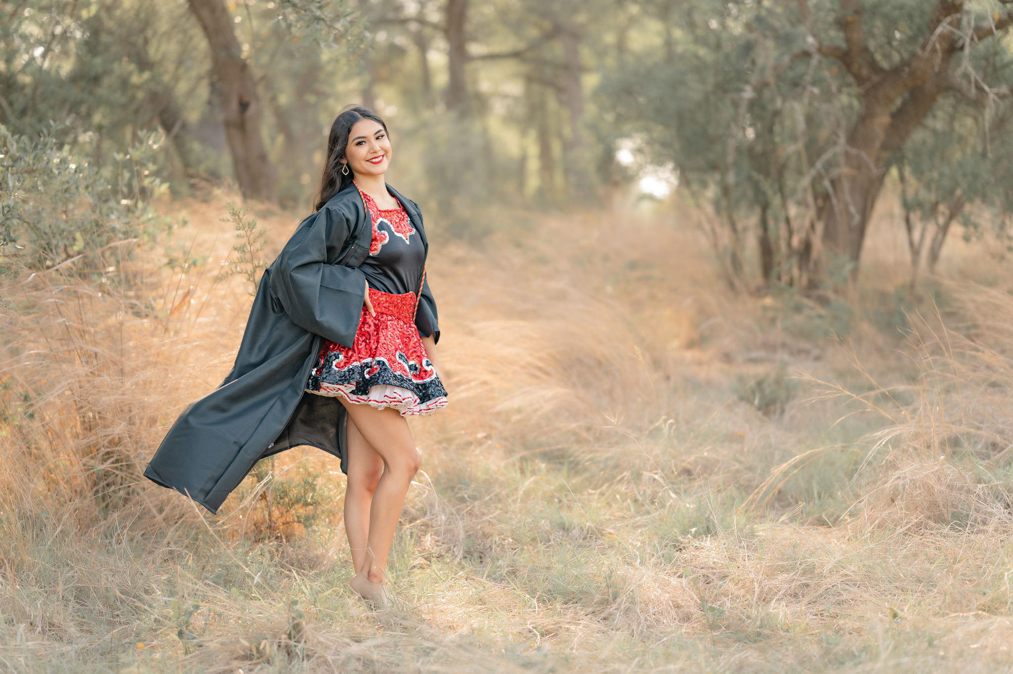A senior girl in her dance uniform and graduation gown stands in the golden grasses at the Cibolo Center for Conservation.