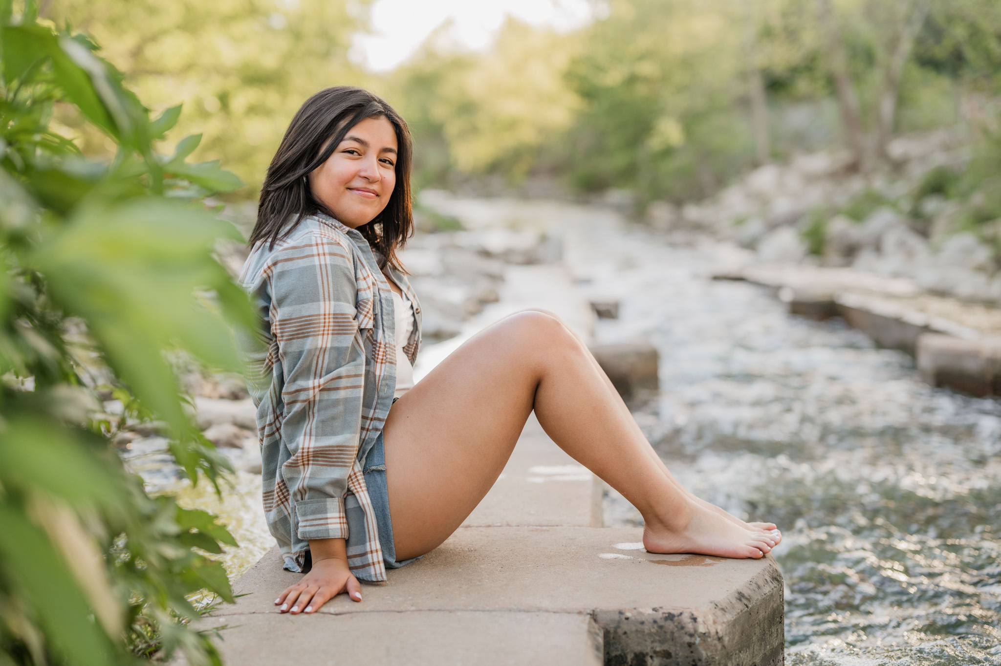 A girl sits along the edge of the river at Confluence Park in San Antonio and smiles at the camera.