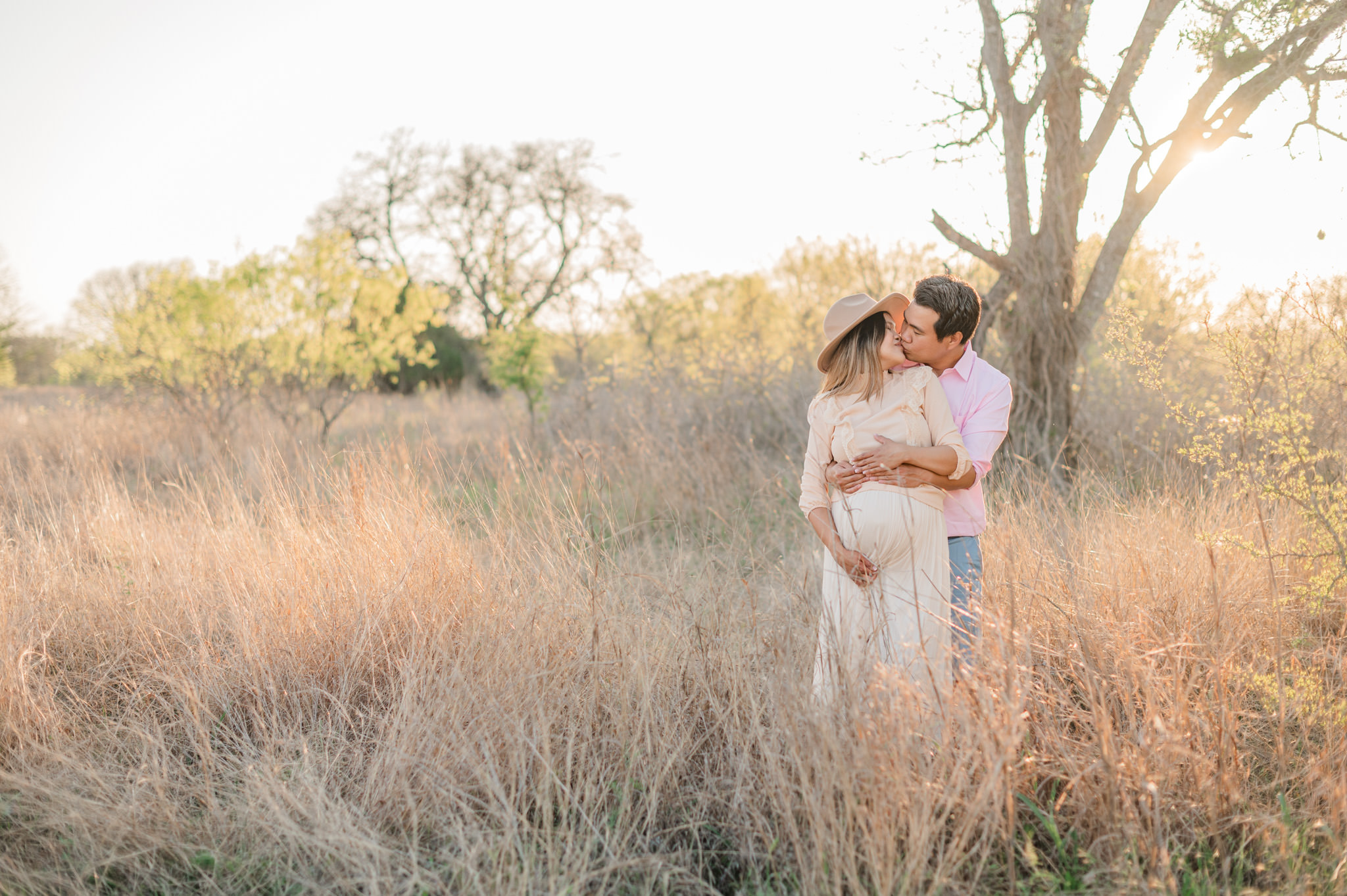 Maternity picture of a man and wife kissing in the golden grass at Crescent Bend Nature Center in Schertz, Texas.