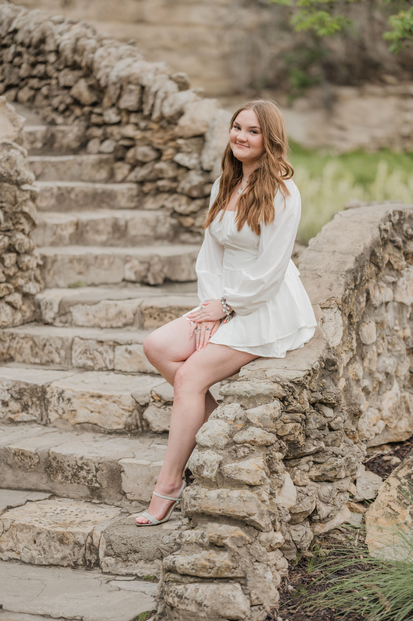 A teenager in a white dress and heels sits on the side of a stone bridge at San Antonio's Japanese Tea Garden.