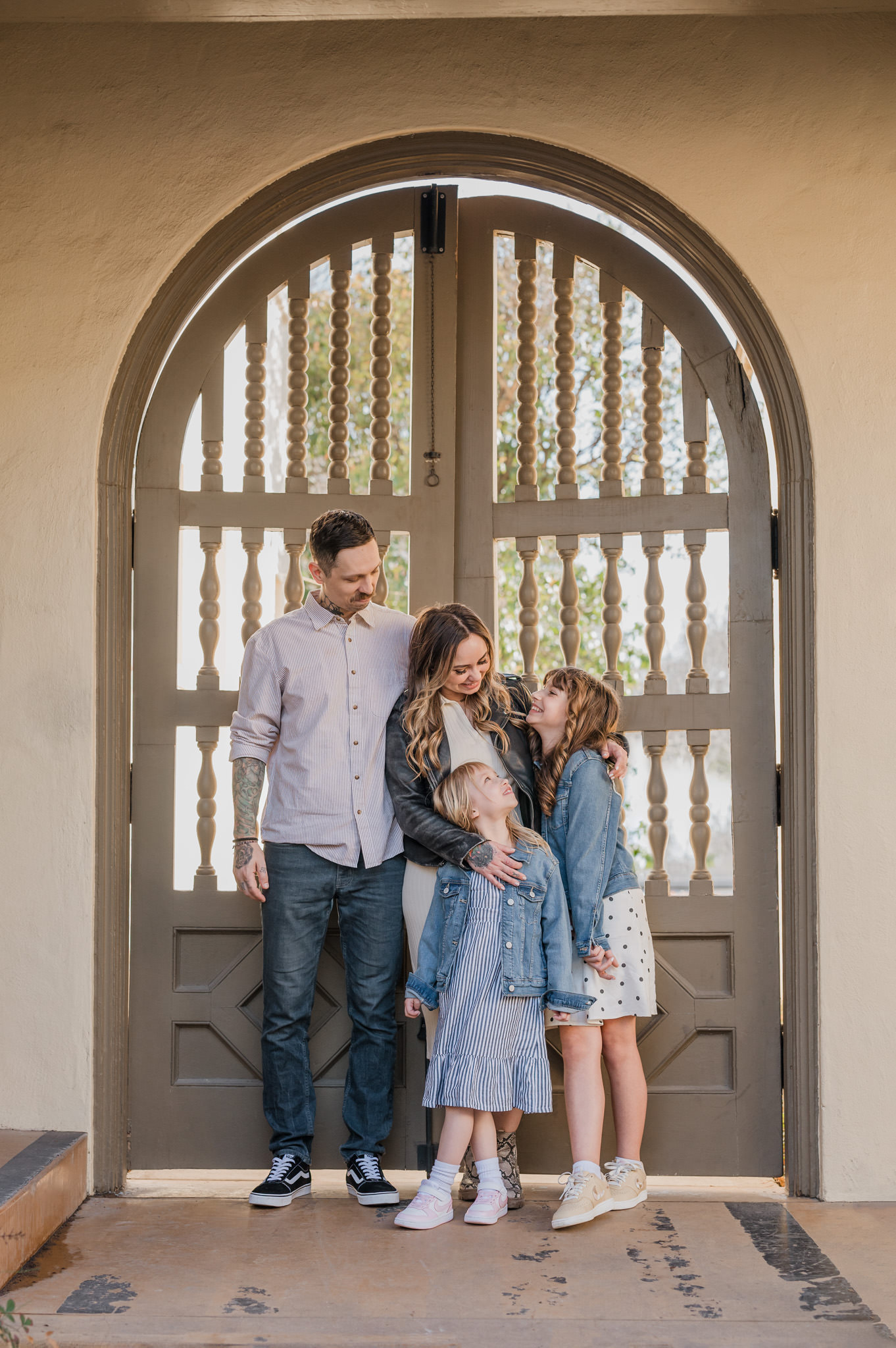 A young family interacts and laughs together. They are standing in front of a beautiful arched doorway on the grounds of Landa Library in San Antonio.