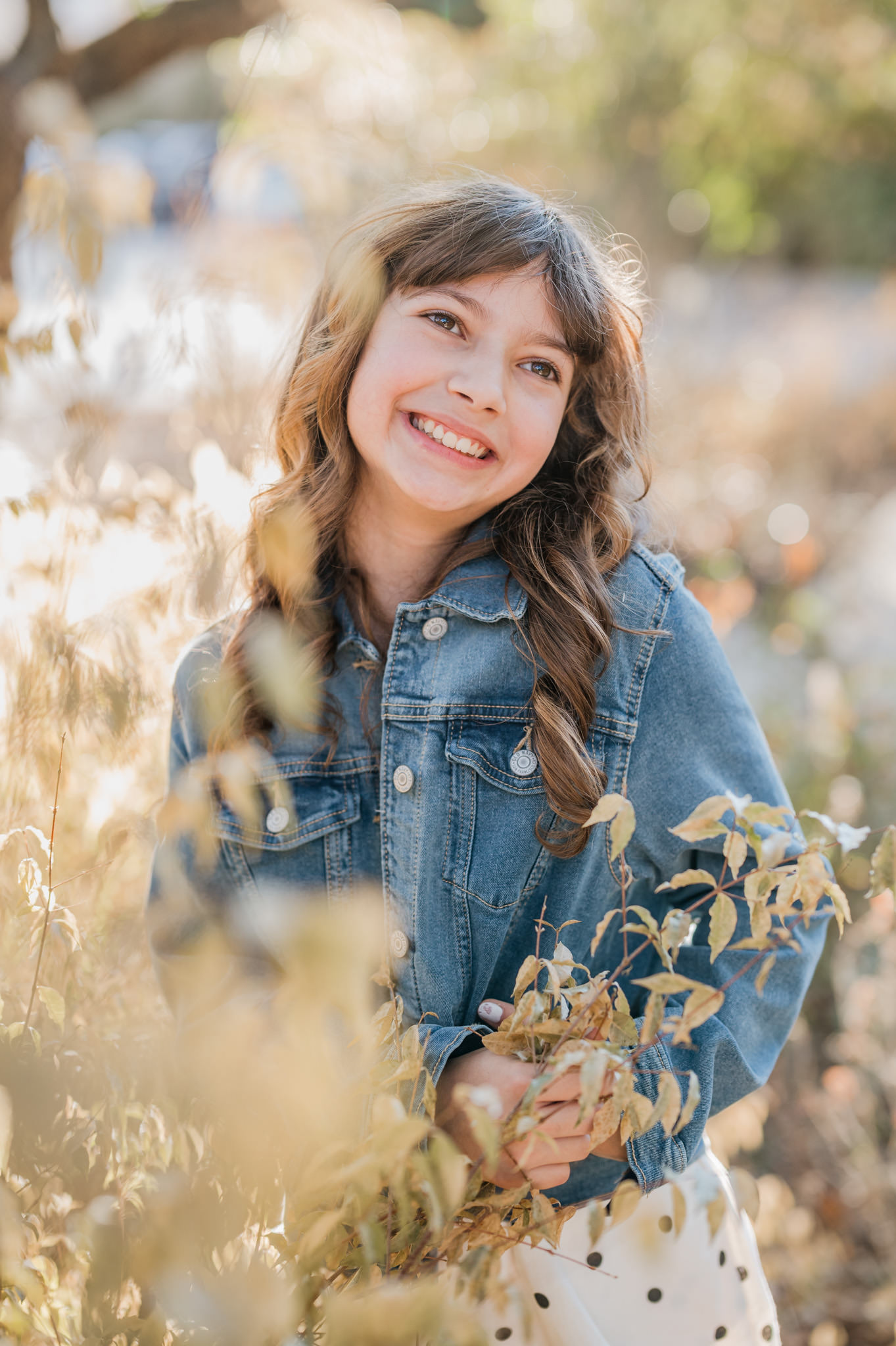 Portrait of a young girl smiling off camera. She's surrounded by foliage at Landa Park Conservancy. 