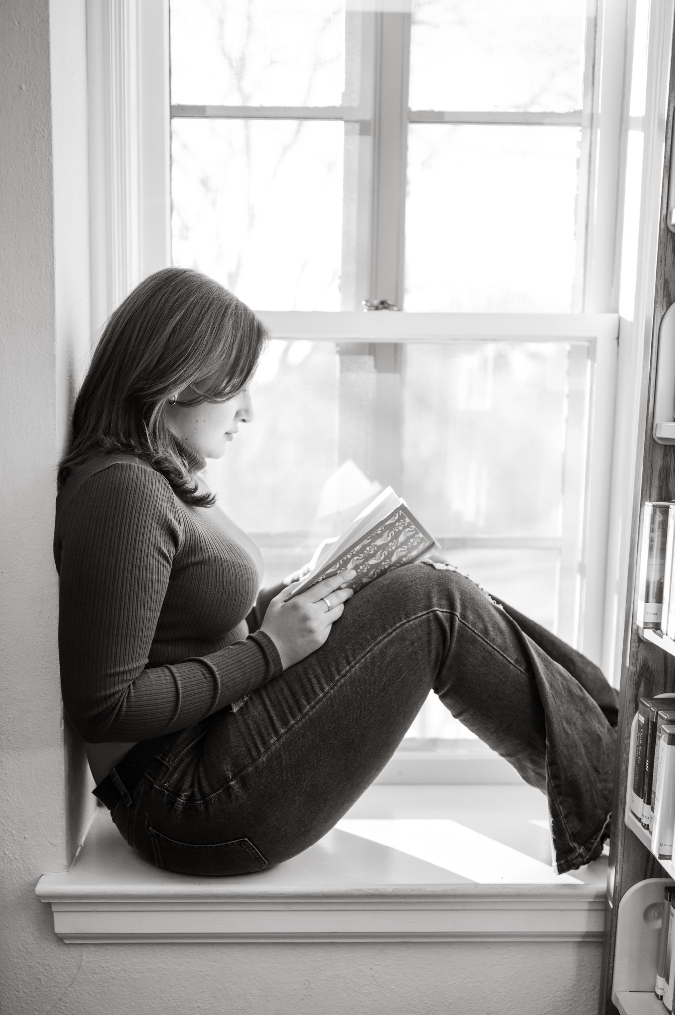 Black and white portrait of a girl curled up in a window in Landa Library, engrossed in a novel. 