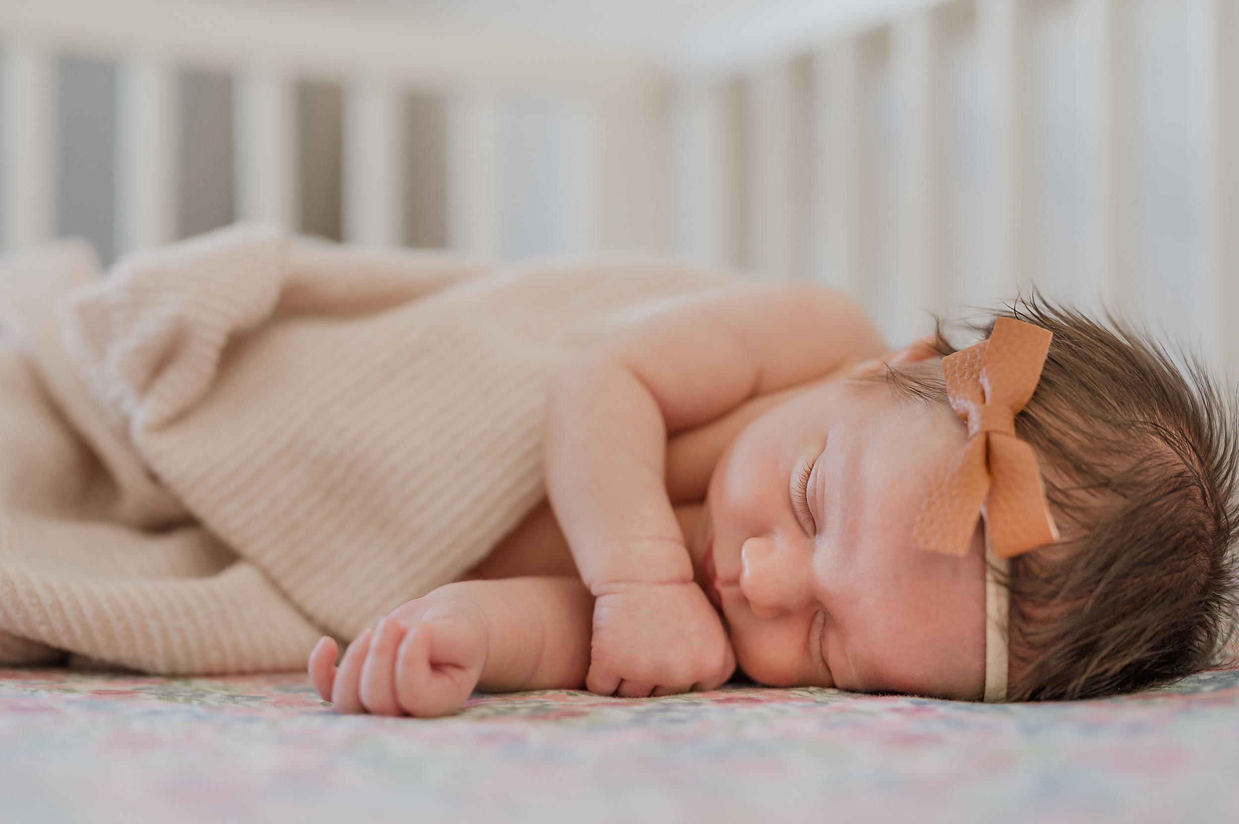 A newborn baby sleeps on her side in a leather bow in a crib nursery couture san antonio
