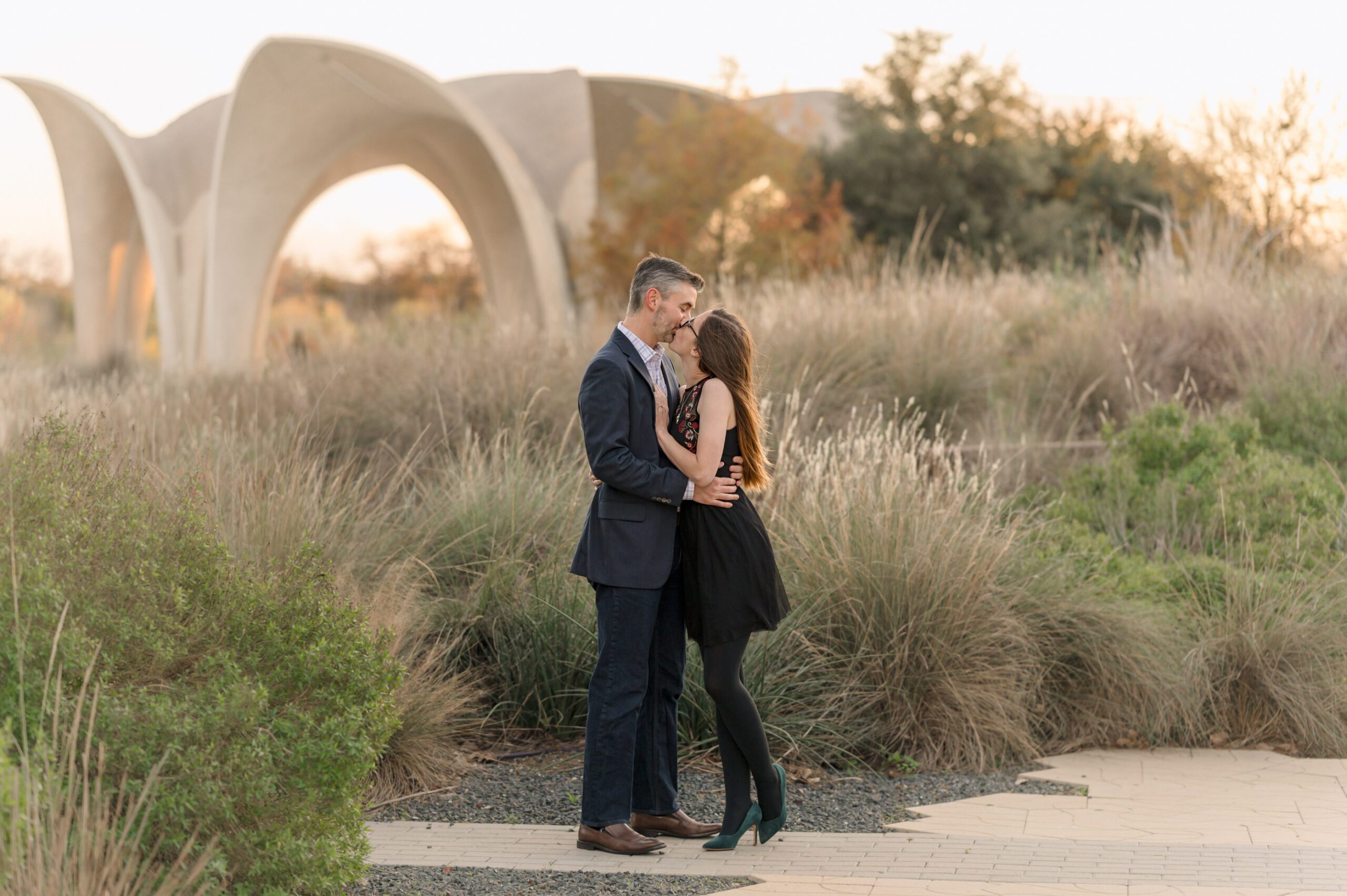 Pull-back images of a couple at Confluence Park. The concrete petals glow in the sunset behind them. 