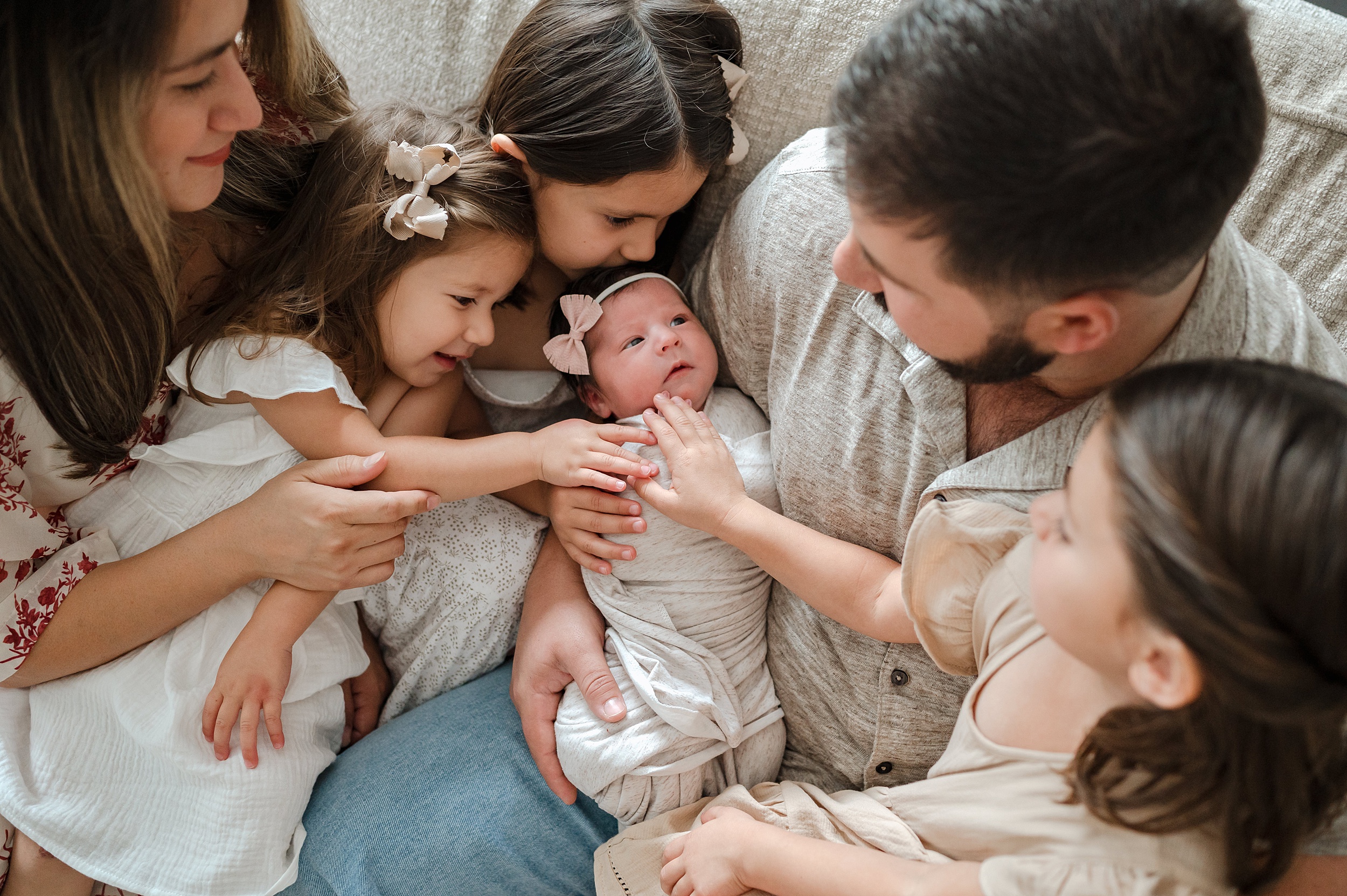 Dad holds his newborn daughter while his wife and three other daughters lean in and place hands on her