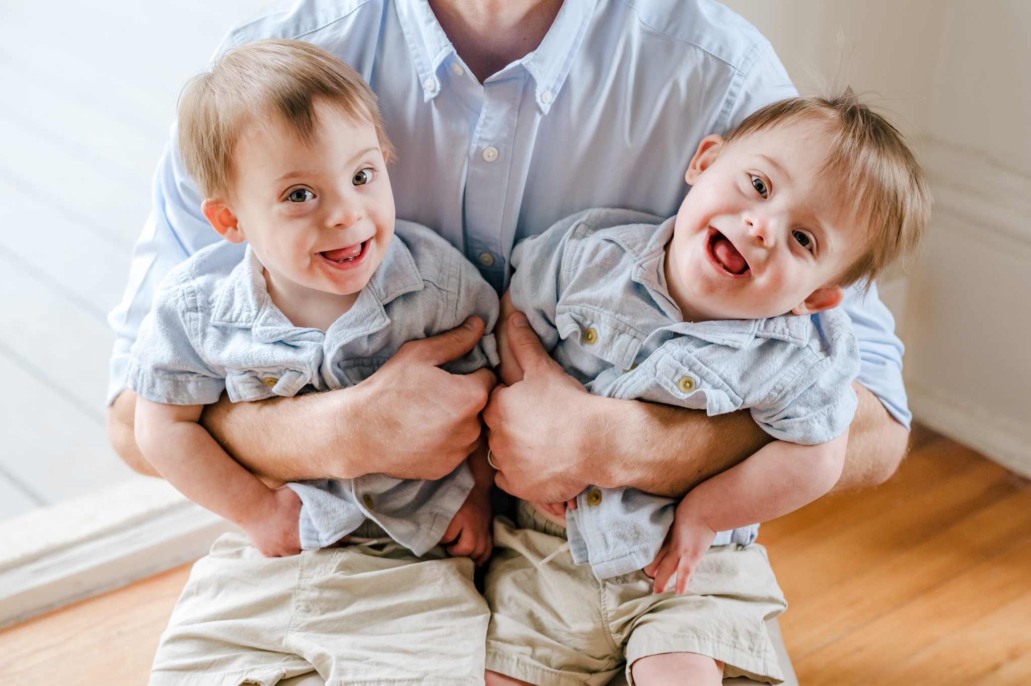 Identical twins with Down syndrome sit on their dad's lap and smile at the camera. Morgan's Wonderland is a great resource for special needs families in South Texas.