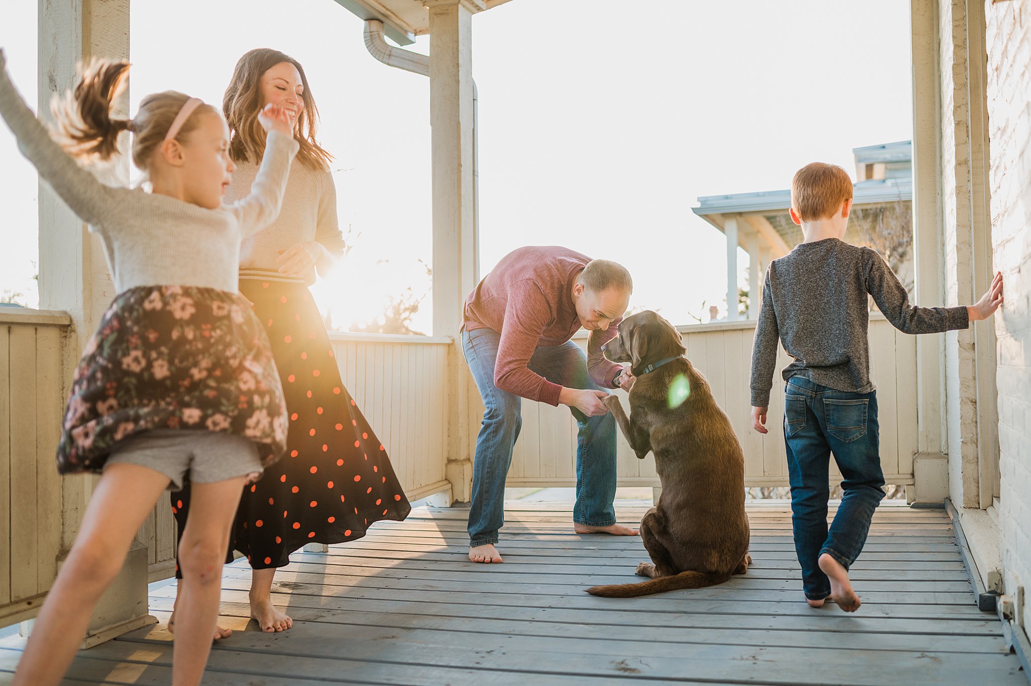 A family of four play on a front porch while dad plays with their brown lab dog san antonio pediatricians