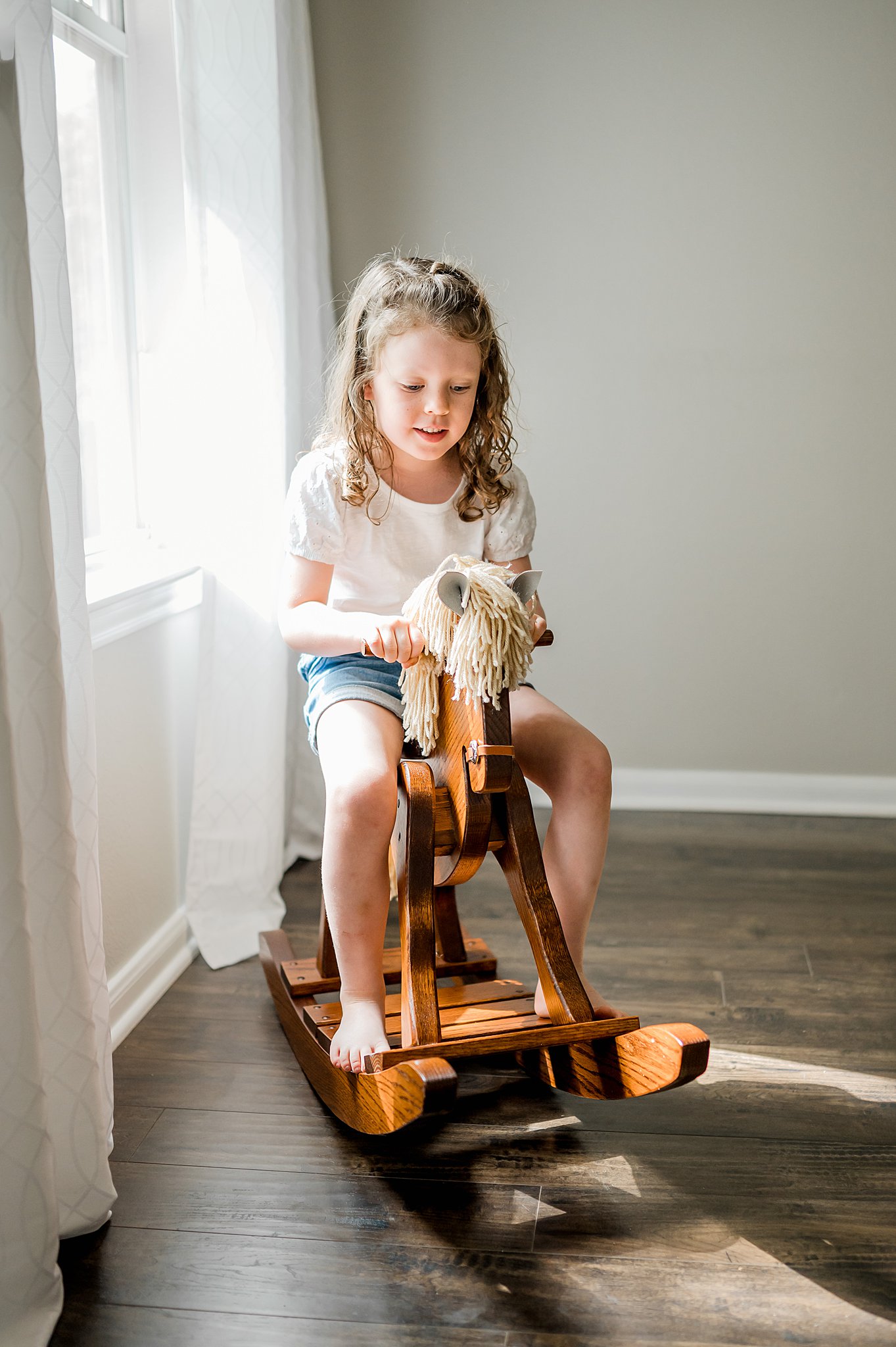 A young girl in a white shirt plays on a wooden rocking horse san antonio toy stores