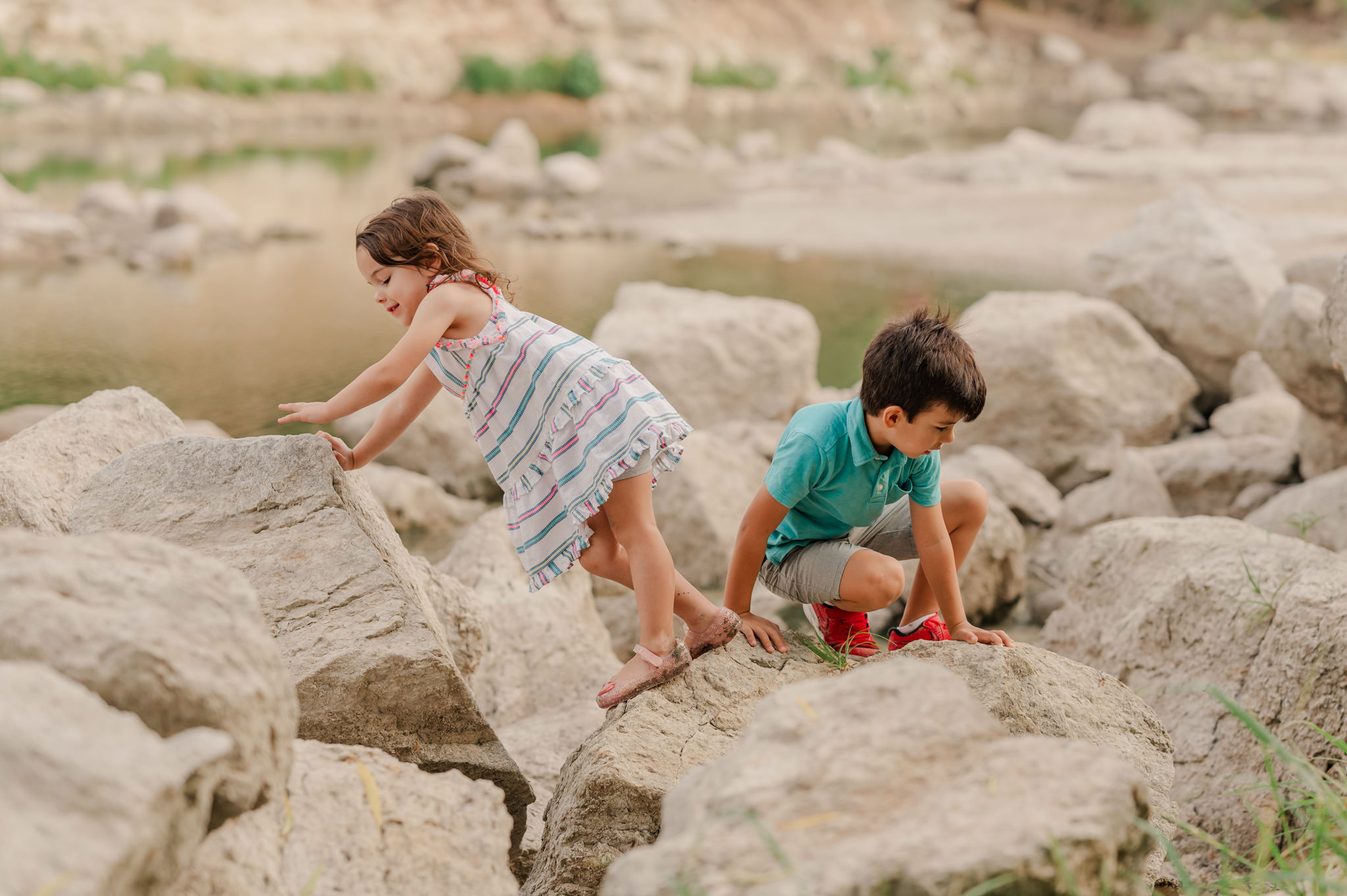 Boy and girl climb on rocks by the water. 