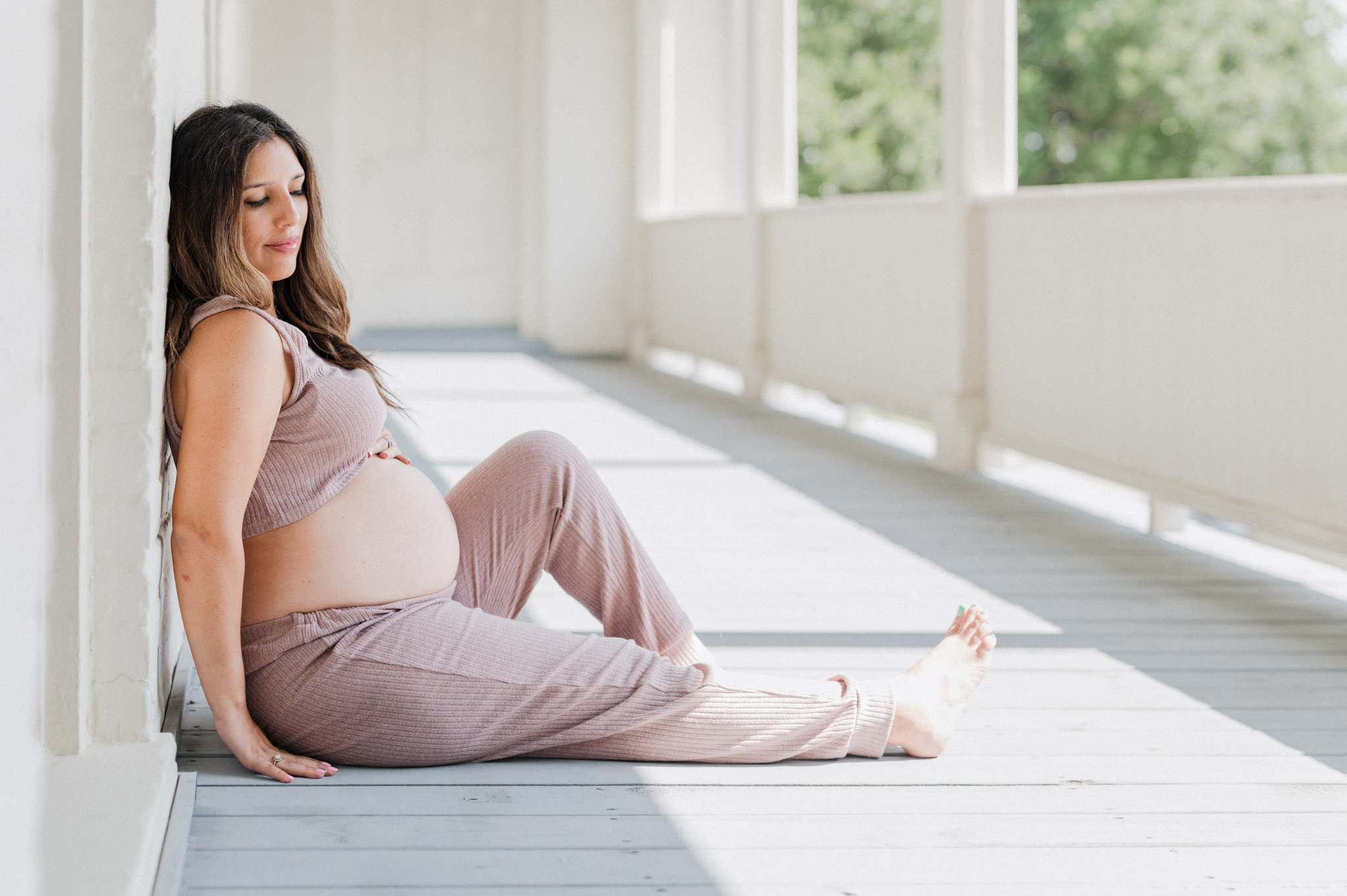 A mother to be in purple pajamas sits on a porch with her bump exposed acacia obgyn