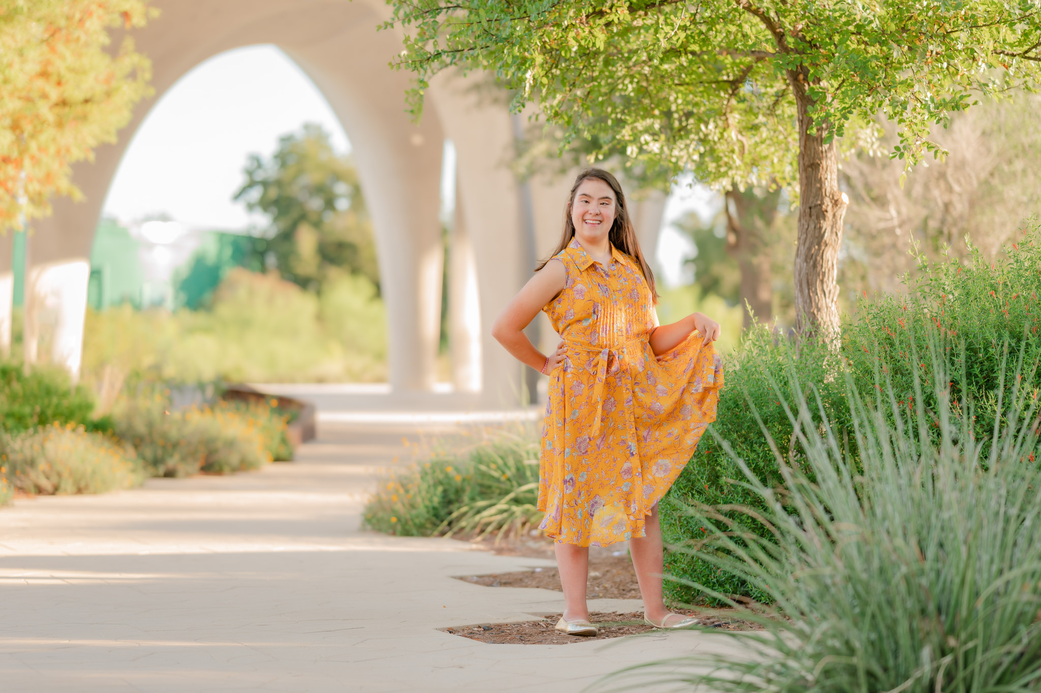A teen girl with Down syndrome wears a springy yellow dress and swishes her skirt around while laughing. Image taken by San Antonio disability photographer Cassey Golden.