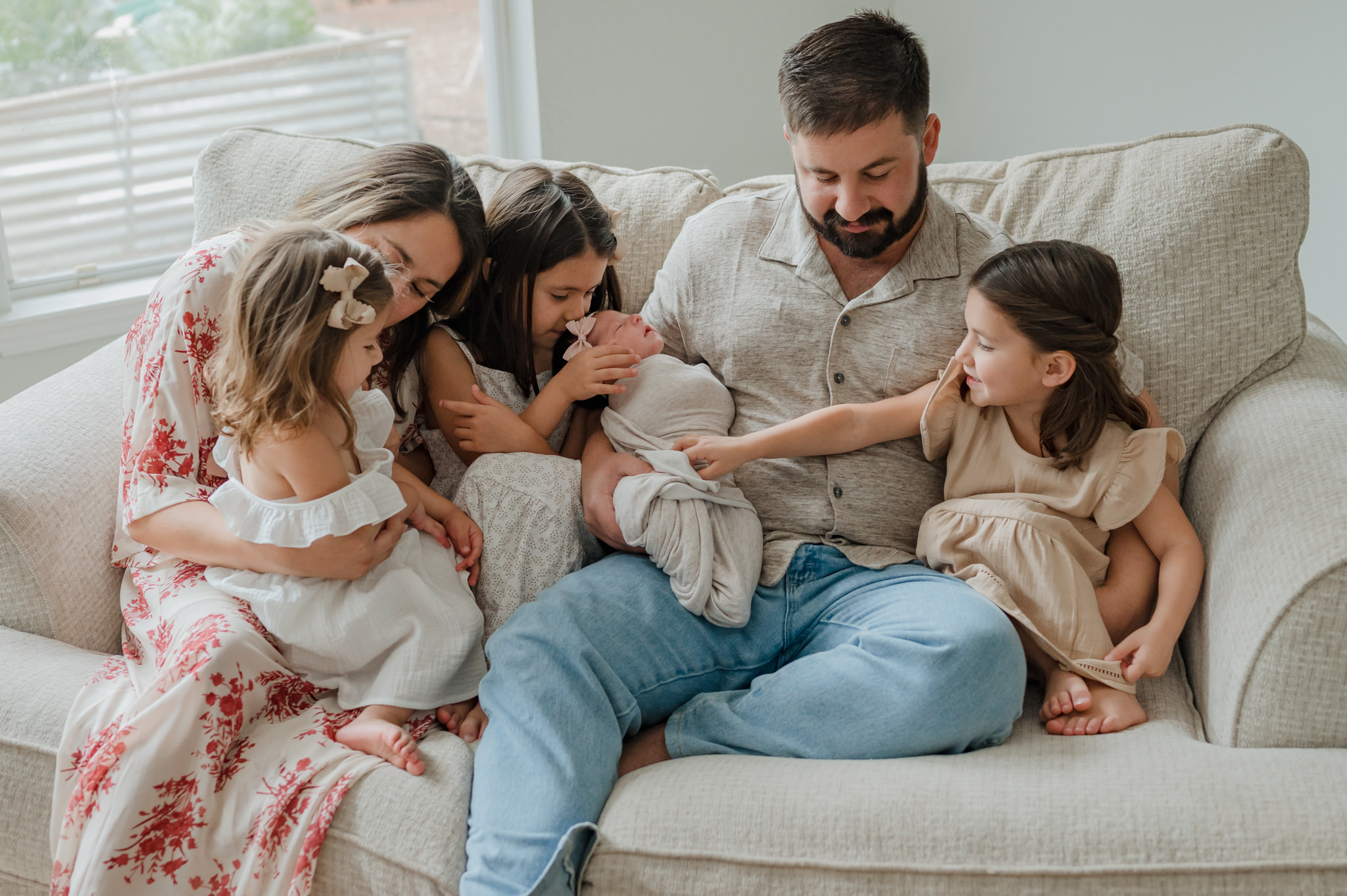 A father sits on a couch holding his newborn baby with his wife and three daughters sit with him playing with the newborn kid to kid san antonio