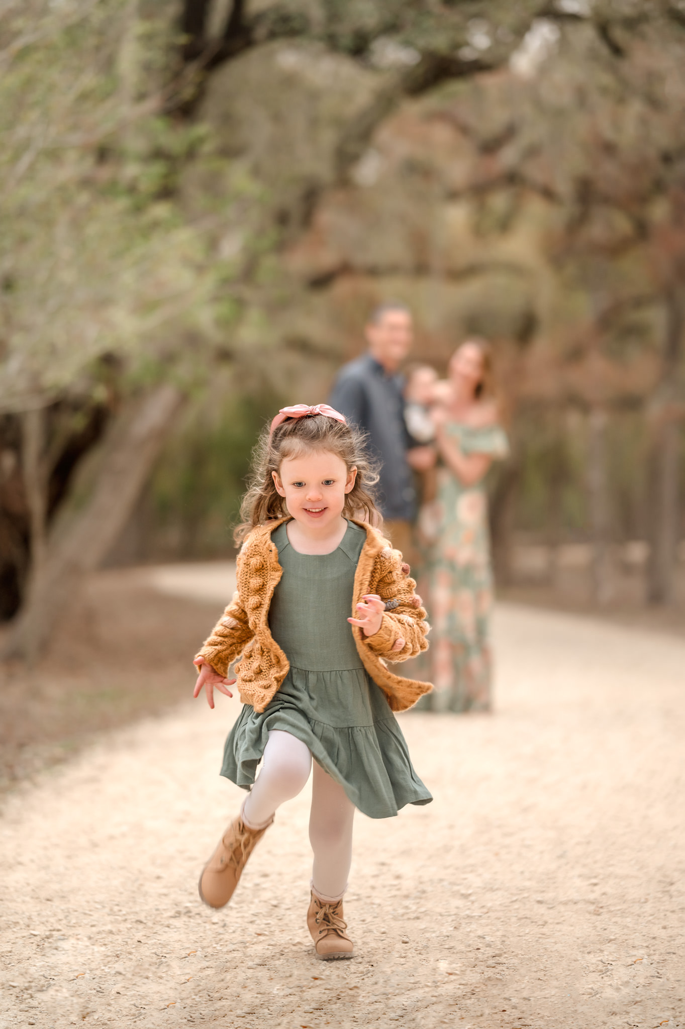 A young girl in a green dress and sweater runs down a park path as her parents watch once upon a child san antonio