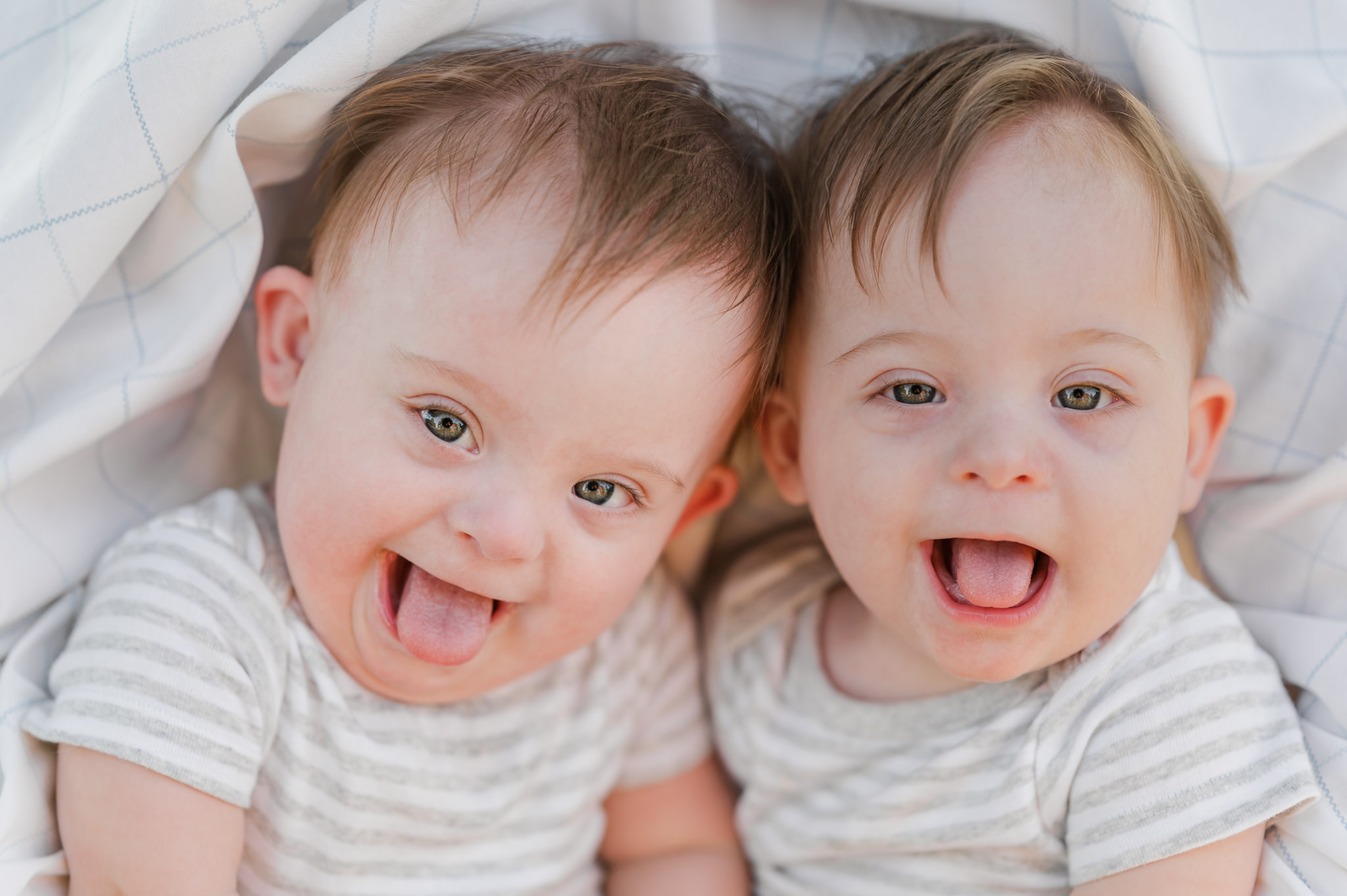 Identical twin boys with Down syndrome sit side by side and have huge smiles for the camera on their first birthday. Picture taken by their mom, San Antonio inclusive photographer Cassey Golden.